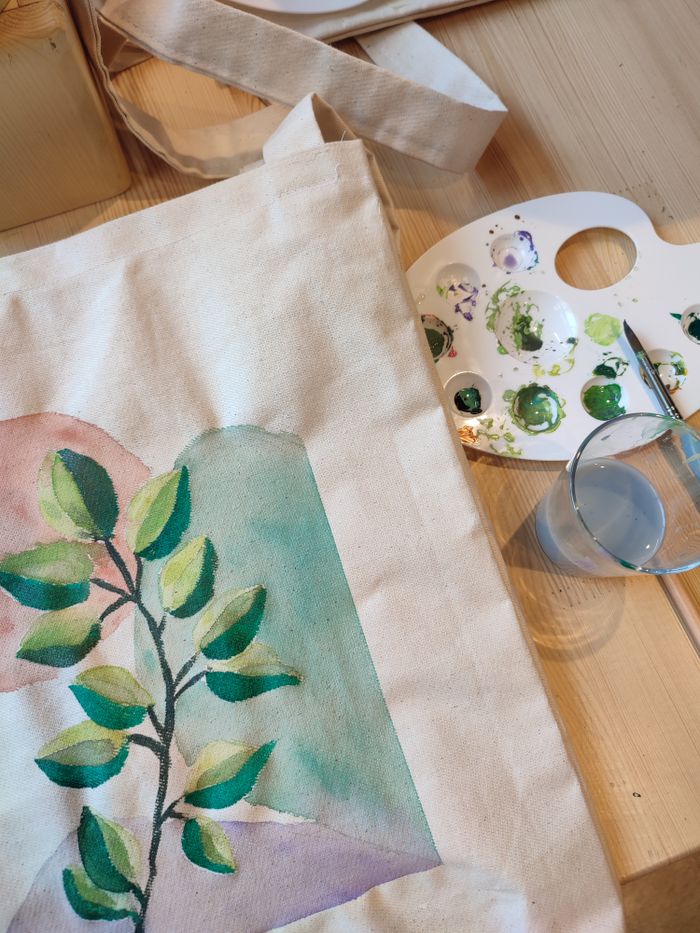 Artistic tote bag with watercolor painting and palette, showcasing creative arts and crafts.
