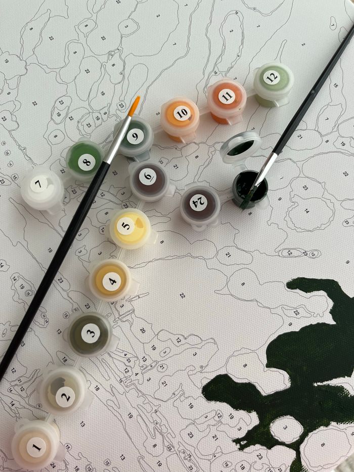 Close-up of a paint by numbers canvas with color pots and brushes.
