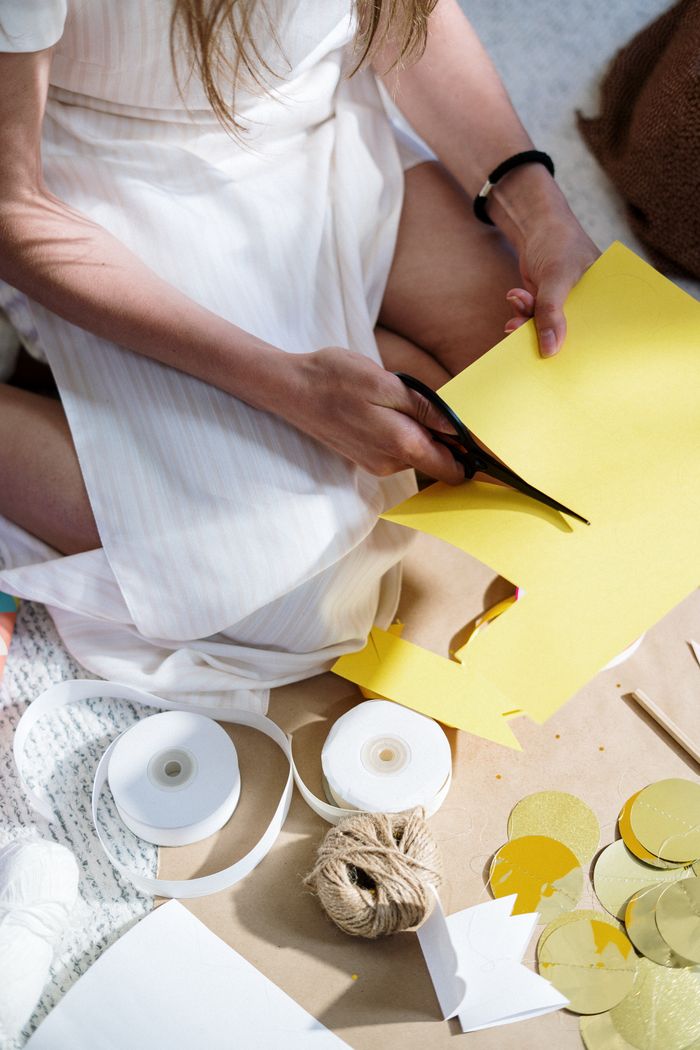 A woman engaged in crafting, cutting yellow paper with scissors amidst various crafting materials.
