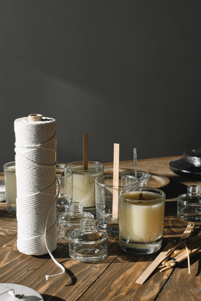 Set of glass molds filled with wax placed on table with thread wick and empty glass vials in light room